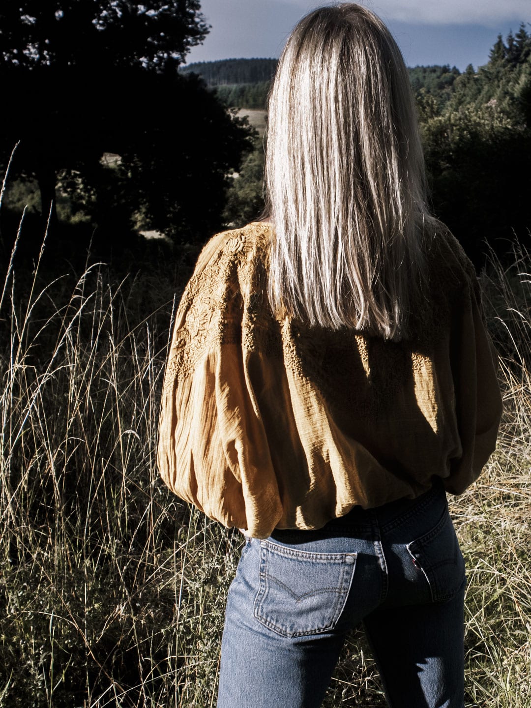 Photo of woman facing away wearing yellow boho peasant top & Levi 501s in French field